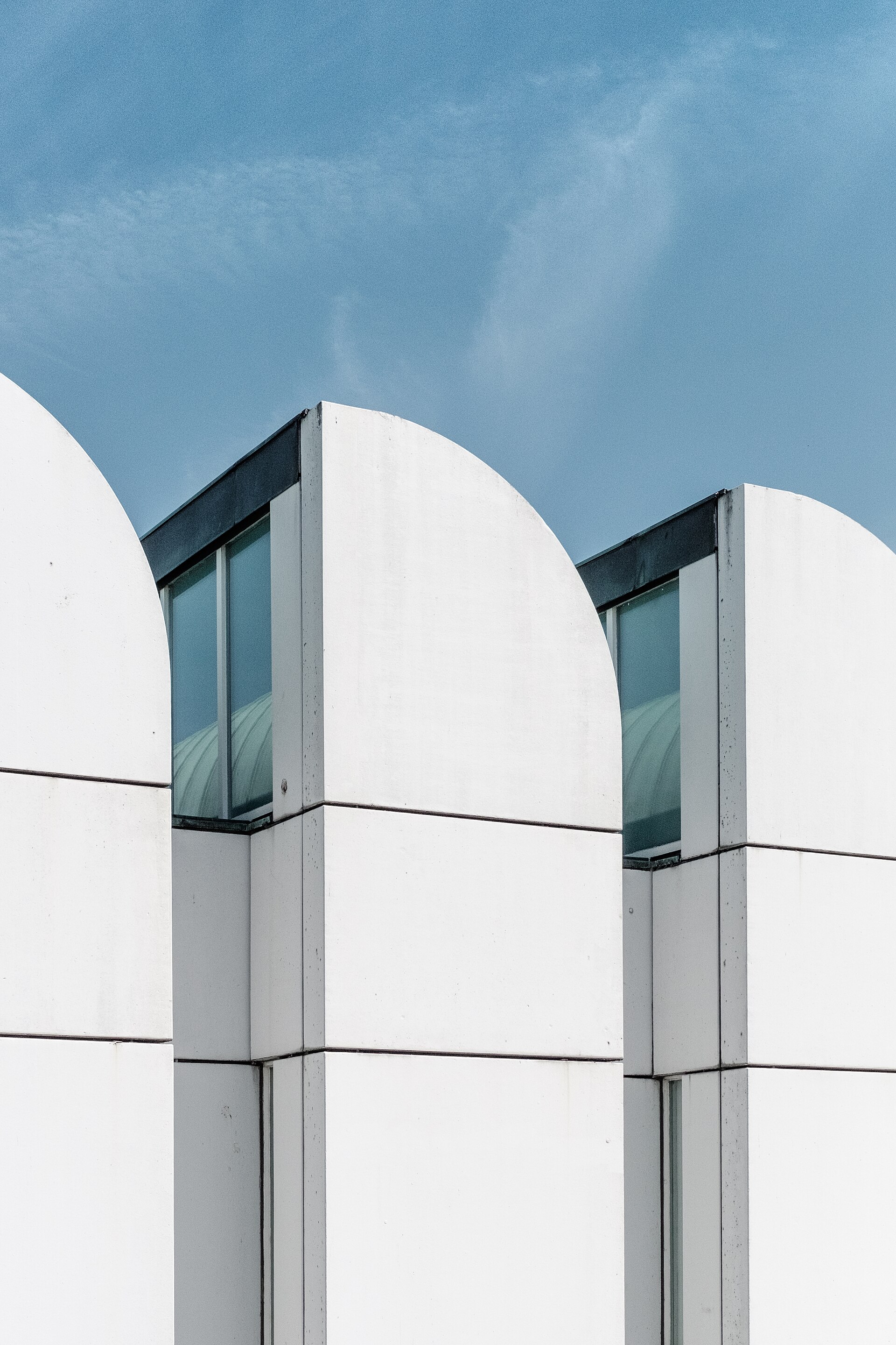 Volumes blancs et verrières inclinées d’un bâtiment moderniste se détachant sur un ciel bleu clair.