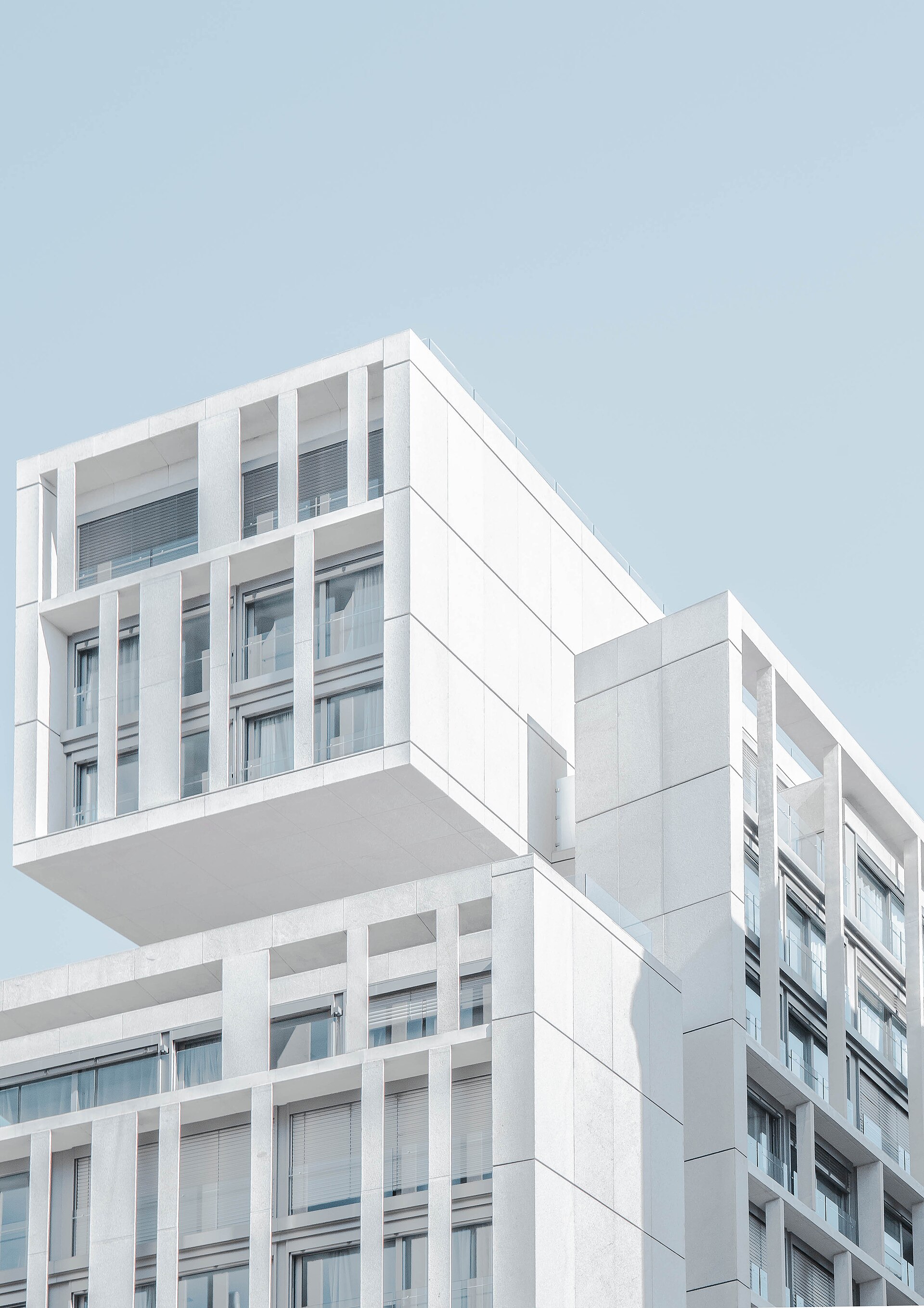 Contre-plongée sur une façade blanche en béton : volumes décalés, loggias profondes et ciel clair.