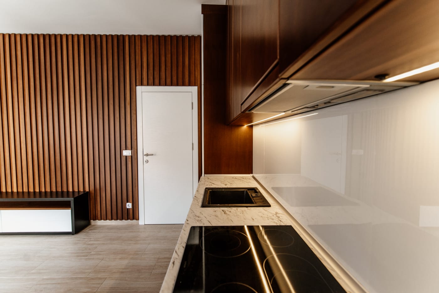 Cuisine contemporaine aux façades en bois sombre, ouverte sur une pièce de vie lumineuse.