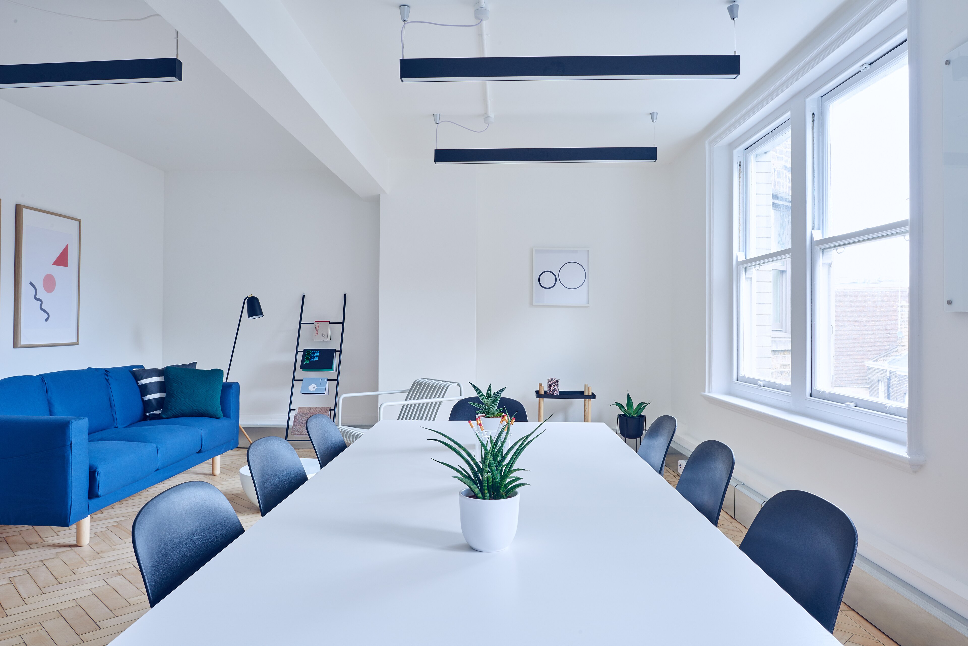 Plateau de bureaux clair : longue table de réunion, plafond technique et fenêtres hautes.