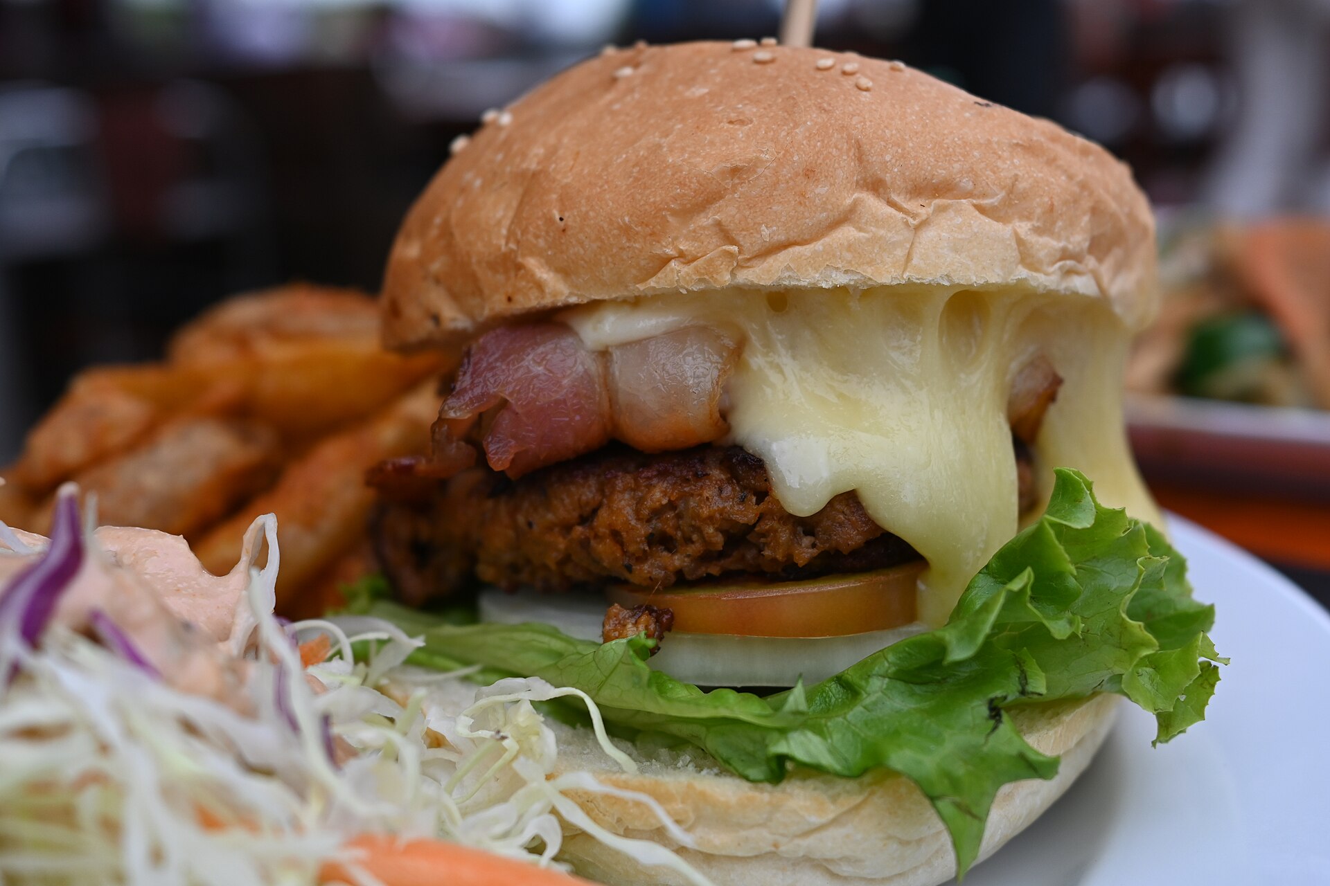 Burger de poulet pané extra-croustillant nappé de fromage fondu et de bacon, salade et tomate, servi avec des frites.