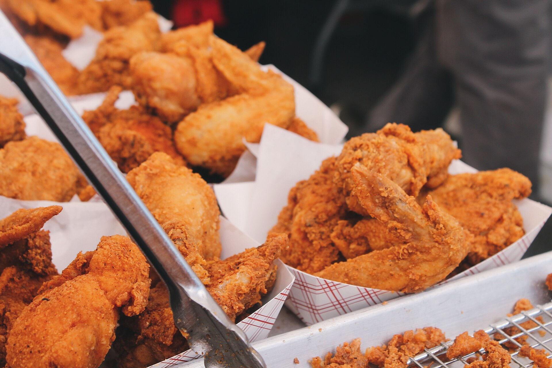 Barquettes de poulet frit encore brûlant, panure épaisse et dorée, alignées derrière une pince de service.