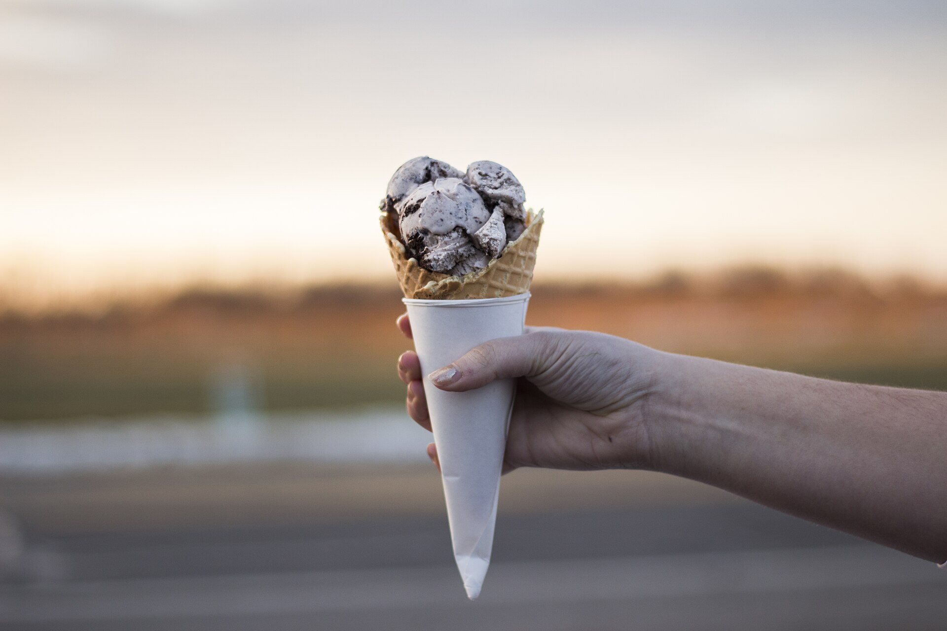 Cornet de glace tenu à bout de bras devant un horizon dégagé, dans la lumière de fin de journée.