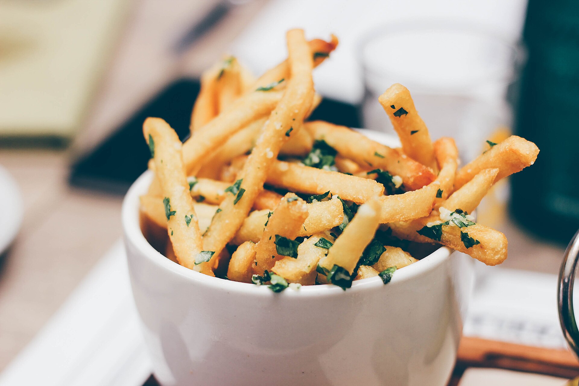 Bol blanc rempli de frites fines dorées, parsemées de persil haché et de sel.