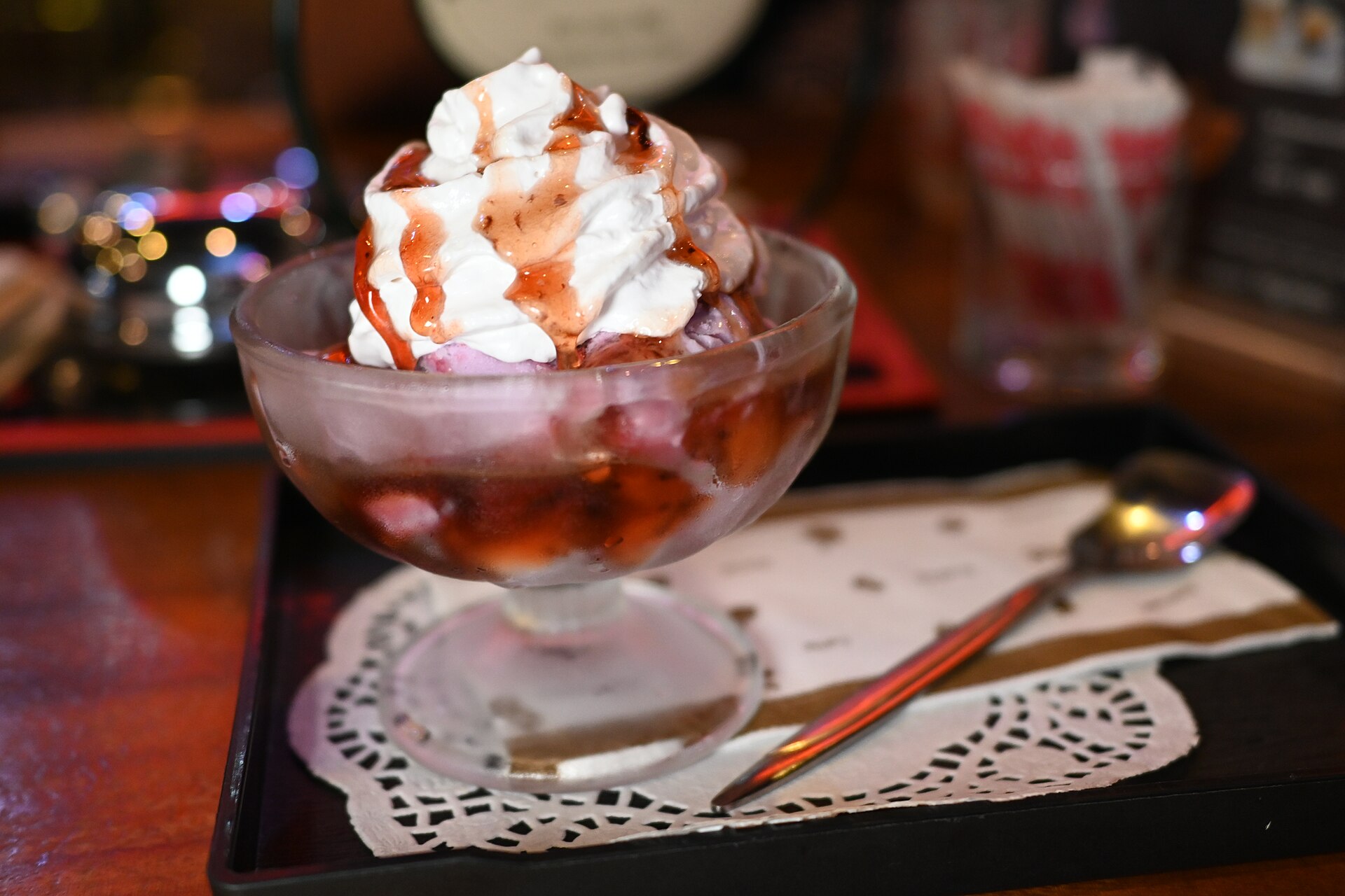 Coupe glacée à la fraise surmontée de chantilly et d'un filet de coulis, posée sur un plateau sombre.