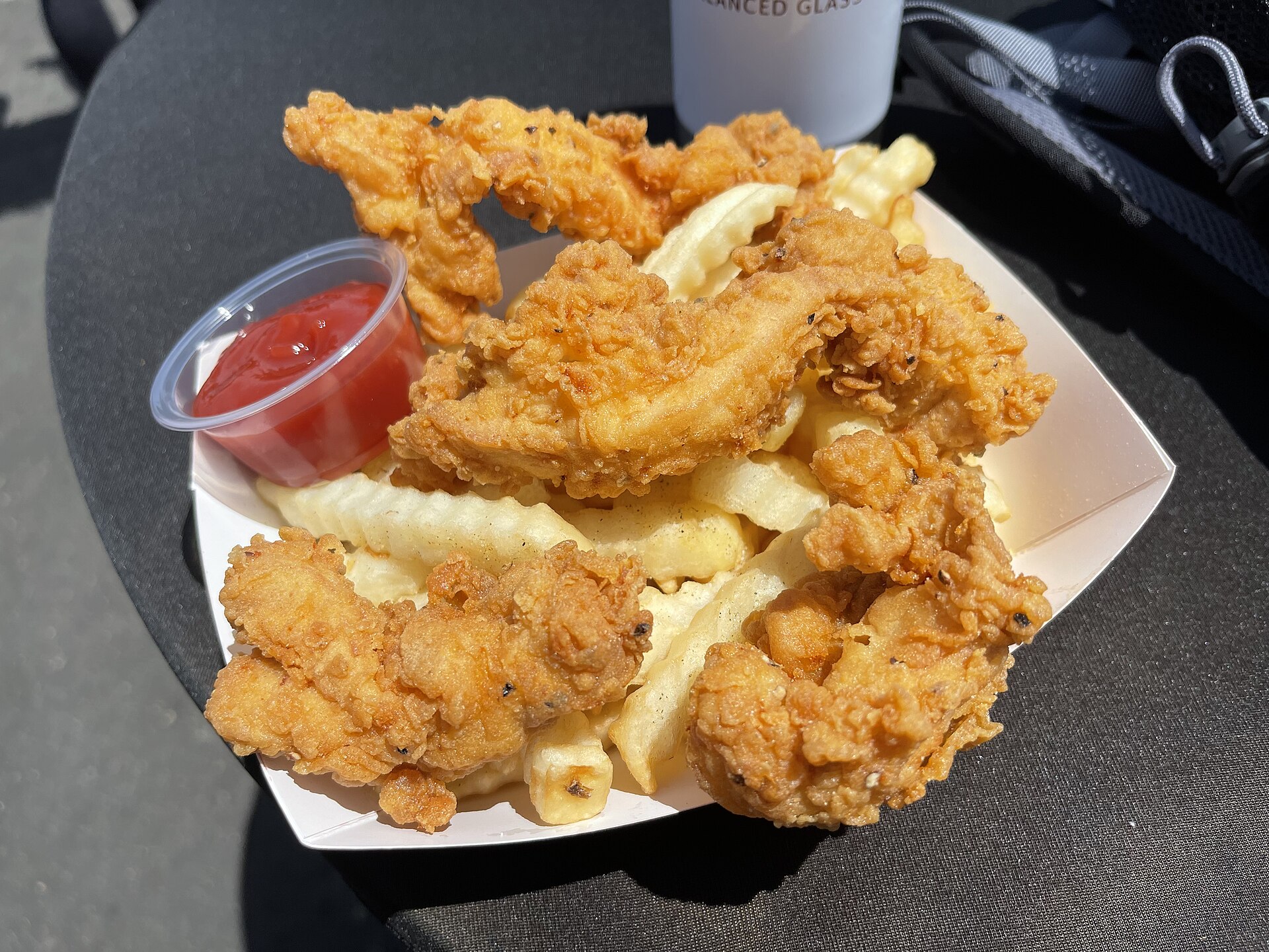 Barquette de tenders de poulet croustillants posés sur un lit de frites ondulées, avec une coupelle de sauce tomate.